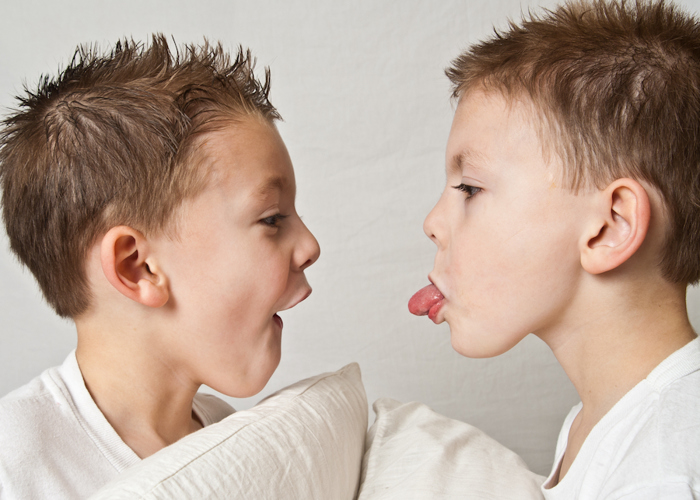 Twin boys, one sticking his tongue out.