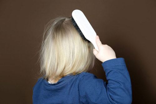 A blonde child brushing their hair.