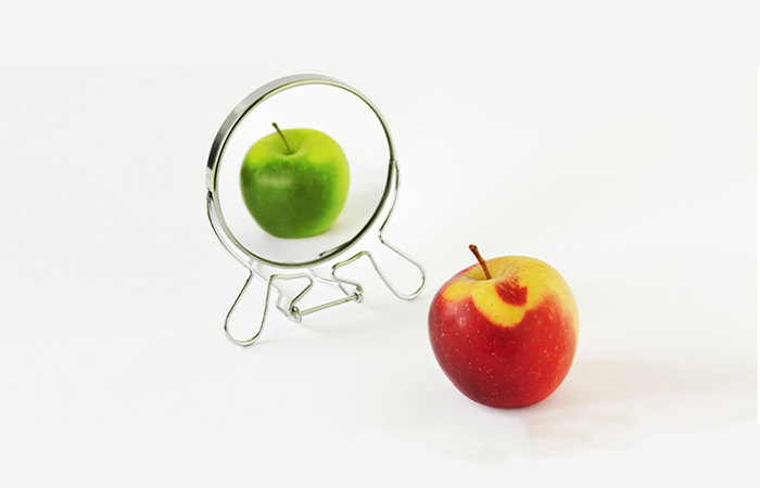 A red and green apple in front of a mirror.