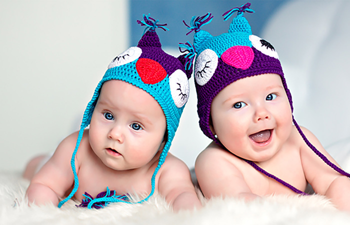 Newborn twins wearing owl hats.