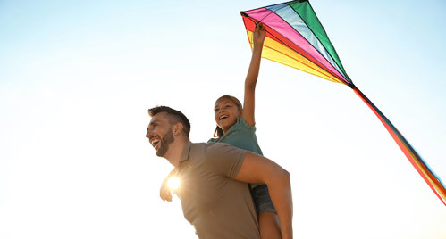 Father and daughter flying a rainbow-colored kite.